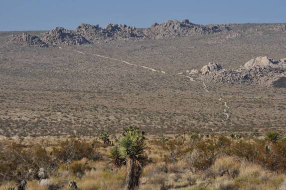 Lá longe, estrada de terra cruza a magnífica paisagem do Joshua Tree National Park, região de Pioneertown, na Califórnia - Estados Unidos